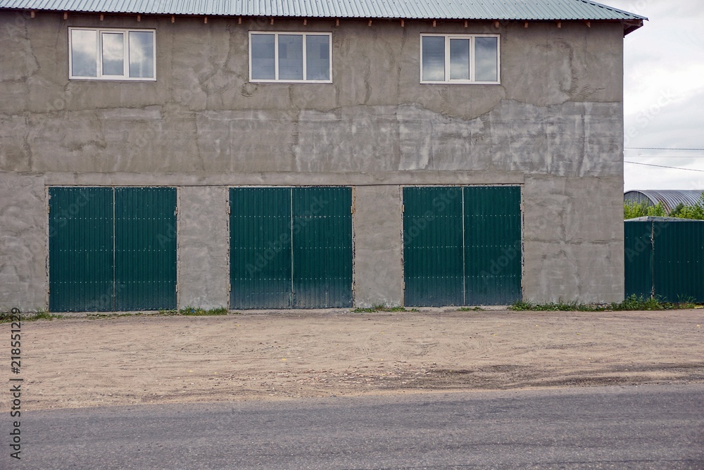 gray wall of a large house with windows and three iron garage gates on the street gray wall of a large house with windows and three iron garage gates on the street
