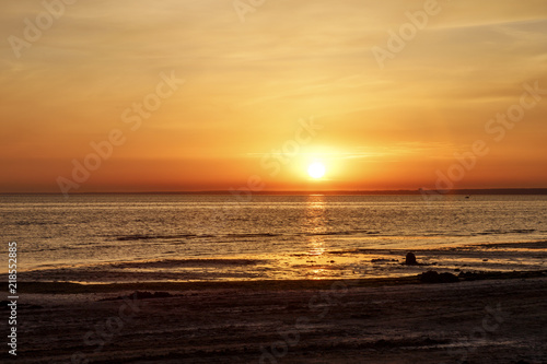 Beautiful sunset over the sea. The sun sets on the water. The sky is painted with golden bright colors. Summer evening. Sunset beach.