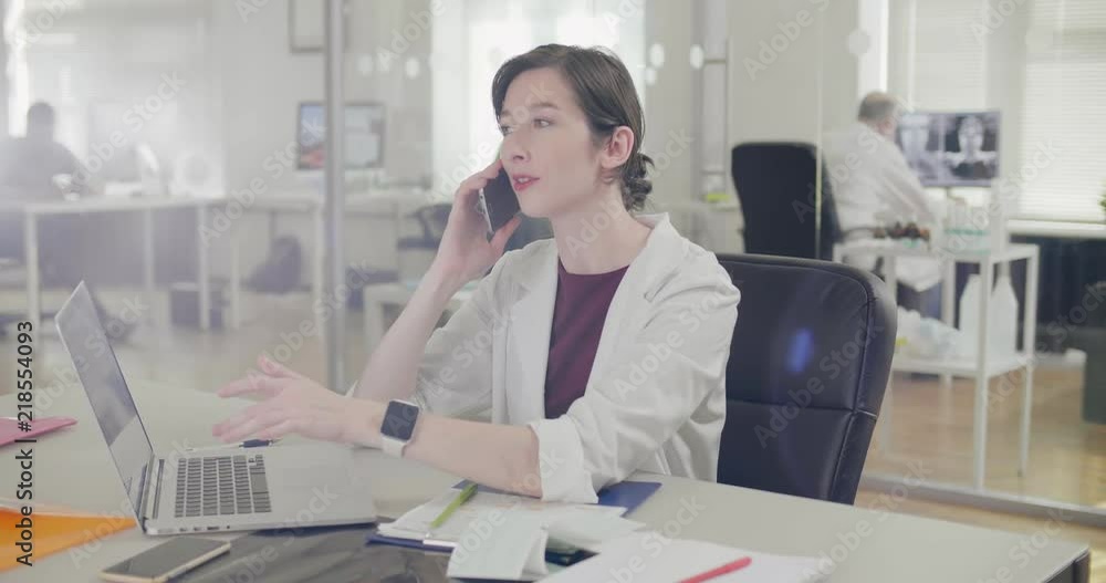 Reception nurse calls client on phone and looks at clock, to remind about time of meeting with doctor. Nurse talking to patient on mobile phone Reception nurse calls client on phone and looks at clock, to remind about time of meeting with doctor. Nurse talking to patient on mobile phone