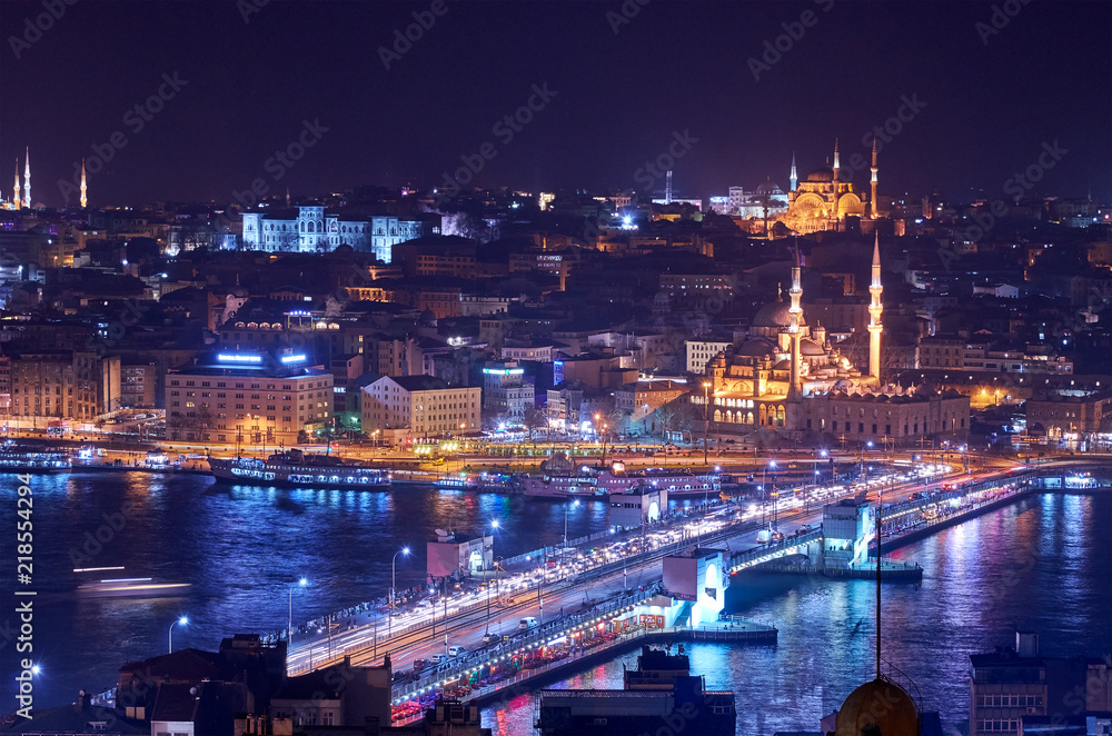 Istanbul's old city at night, with Galata Bridge in the foreground, and the Hagia Sophia and Blue Mosque