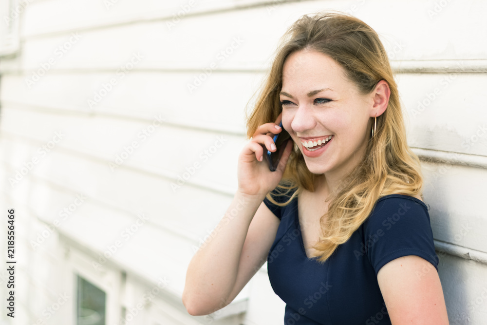 Portrait of a young woman blonde with blue eyes speaking on a mobile outdoors, laughing.