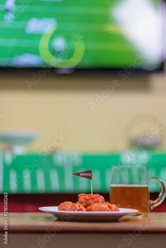 plate of boneless hot wings and beer with sports on TV in background