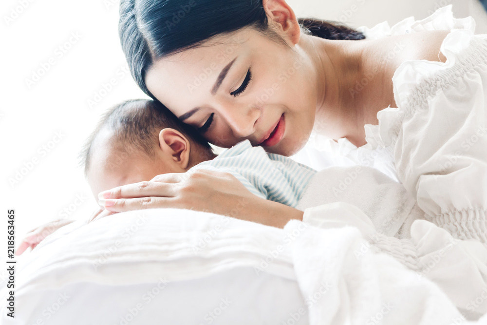 Mother kiss and holding sleeping baby hand on white bed.Love of family concept Mother kiss and holding sleeping baby hand on white bed.Love of family concept