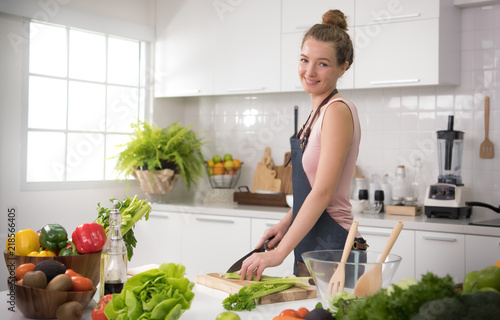 Healthy young woman in a kitchen cutting vegetables and preparing healthy meal and salad