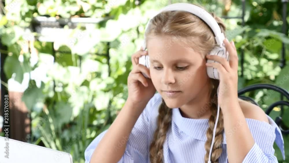 Videoportrait of adorable girl sitting at table with a white notebook, putting headphones on Videoportrait of adorable girl sitting at table with a white notebook, putting headphones on