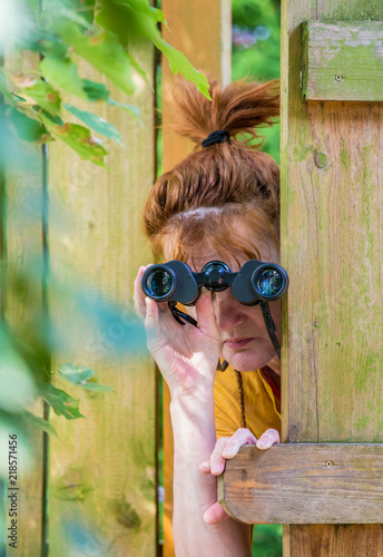 Fotografie eine neugierige Frau blickt mit einem Fernglas durch einen Zaun