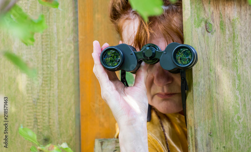 Obraz na plátně eine neugierige Frau blickt mit einem Fernglas durch einen Zaun