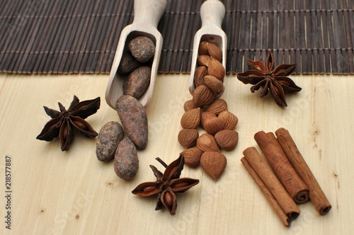 Concept with ingredients for chocolate, cocoa beans, cinnamon, anise, apricot beans on wooden spoons on brown background, side view, selective focus
