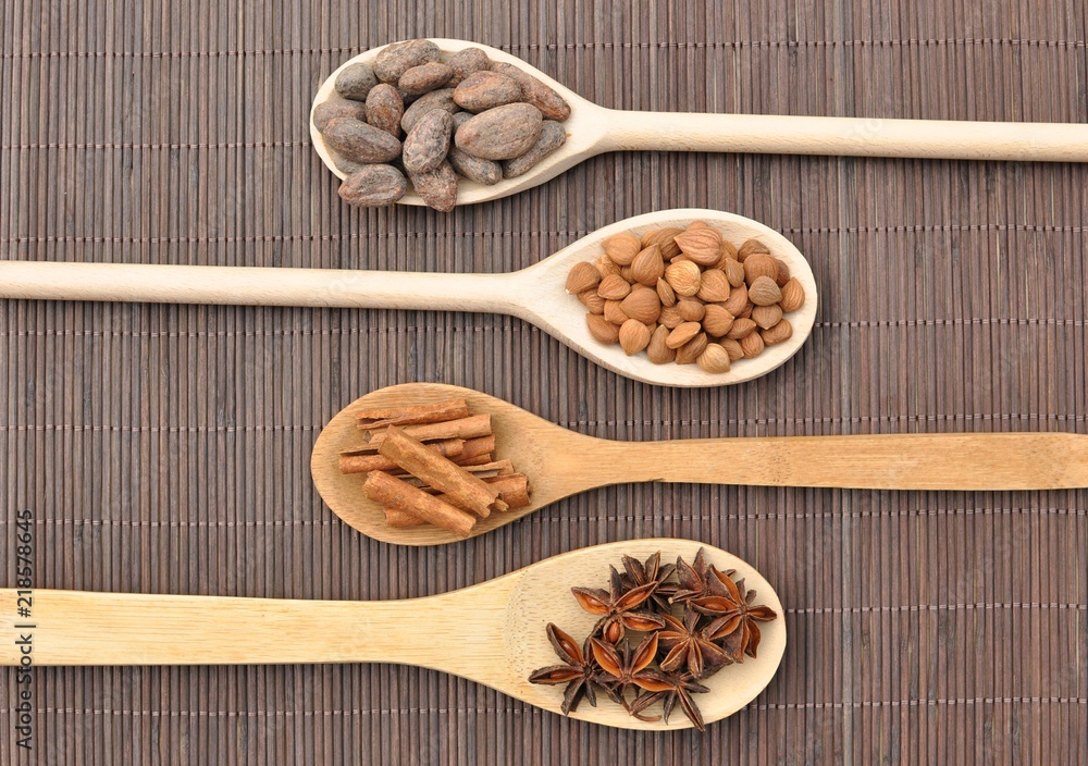 Concept with ingredients for chocolate, cocoa beans, cinnamon, anise, apricot beans on wooden spoons on brown background, top view Concept with ingredients for chocolate, cocoa beans, cinnamon, anise, apricot beans on wooden spoons on brown background, top view