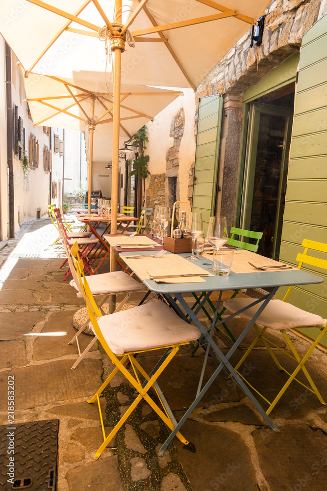 Naklejka premium Small caffee, restaurant in narrow street in a medieval town with colorful tables and chairs