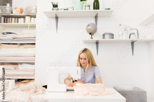 Close-up portrait of young seamstress or dressmaker sews on sewing machine in her own workplace. Sewing hobby, small business or startup concept