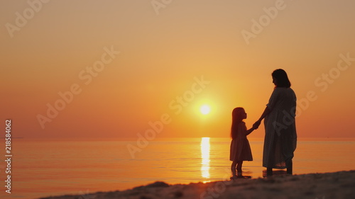 A pregnant woman with a daughter is standing on the beach at sunset. Waiting for the second child