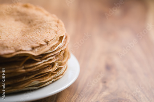 Stack of fresh hot crepes or blinis on wood table with copy space