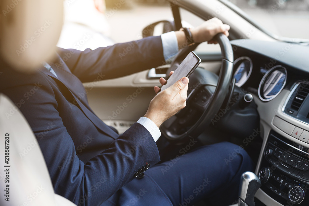 a businessman driving a prestigious car holds a mobile phone in his hand. Hasty life a businessman driving a prestigious car holds a mobile phone in his hand. Hasty life