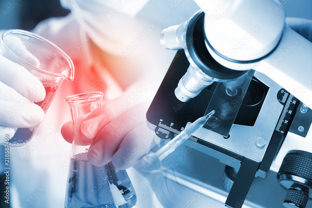 Fototapeta premium Science background with microscope in science laboratory with red liquid and dropper for testing. Technician dripping red water on slide glass in science lab.