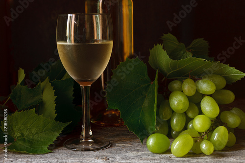 Tableau sur toile Green grapes with leaves, glass, bottle of white wine on vintage wooden background