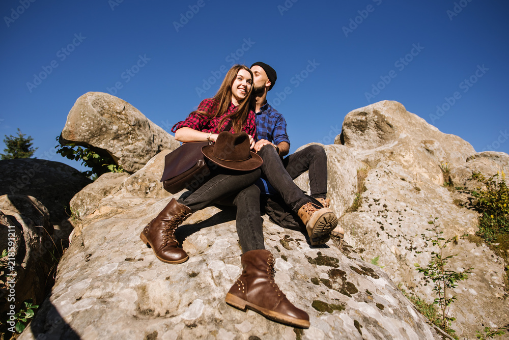 Naklejka premium A hipster traveler couple sitting together on the rocks at the mountains