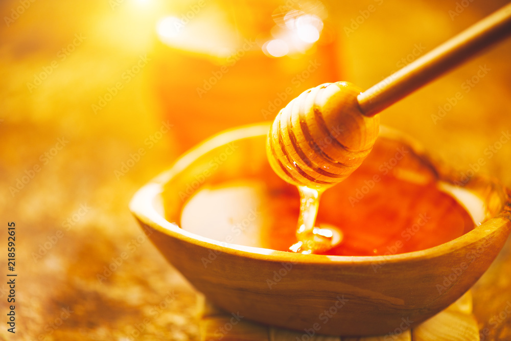 Honey dripping from honey dipper in wooden bowl. Healthy organic thick honey pouring from the wooden honey spoon closeup Honey dripping from honey dipper in wooden bowl. Healthy organic thick honey pouring from the wooden honey spoon closeup