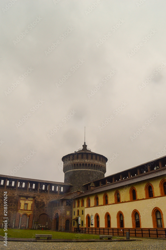 Fototapeta premium A rainy view of a castle watch tower with clouds and yellow buildings