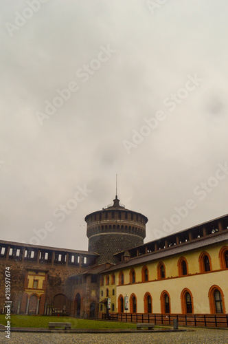 A rainy view of a castle watch tower with clouds and yellow buildings
