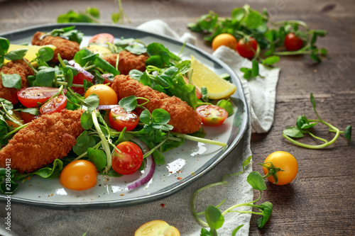 Fresh salad with chicken nuggets, cherry tomatoes and green vegetables in a rustic wooden table