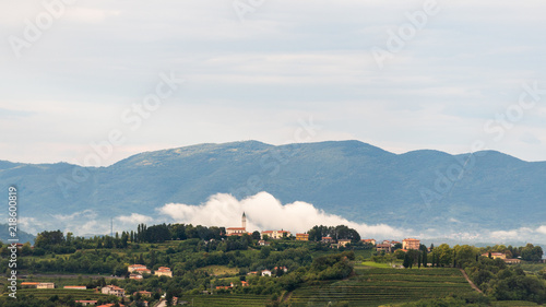 Village of Steverjan, San Floriano del Collio, Italy with church in front of white low white cloud, Goriska Brda, with vineyards and orchards photo
