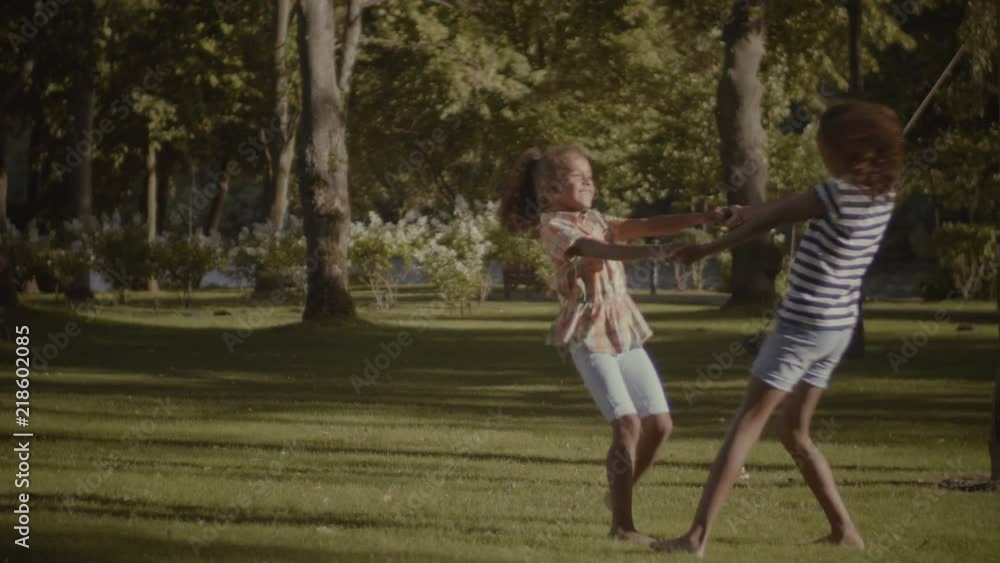 Laughing excited adorable little mixed race sisters holding hands and spinning around in summer park while enjoying leisure togehter. Carefree children having fun and playing in nature. Slow motion. Laughing excited adorable little mixed race sisters holding hands and spinning around in summer park while enjoying leisure togehter. Carefree children having fun and playing in nature. Slow motion.