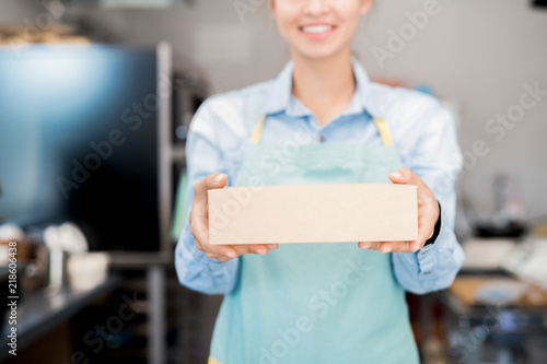 Mid section portrait of unrecognizable woman wearing apron holding box with takeaway food and smiling happily