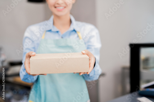 Mid section portrait of unrecognizable woman wearing apron holding box with takeaway food and smiling happily, copy space