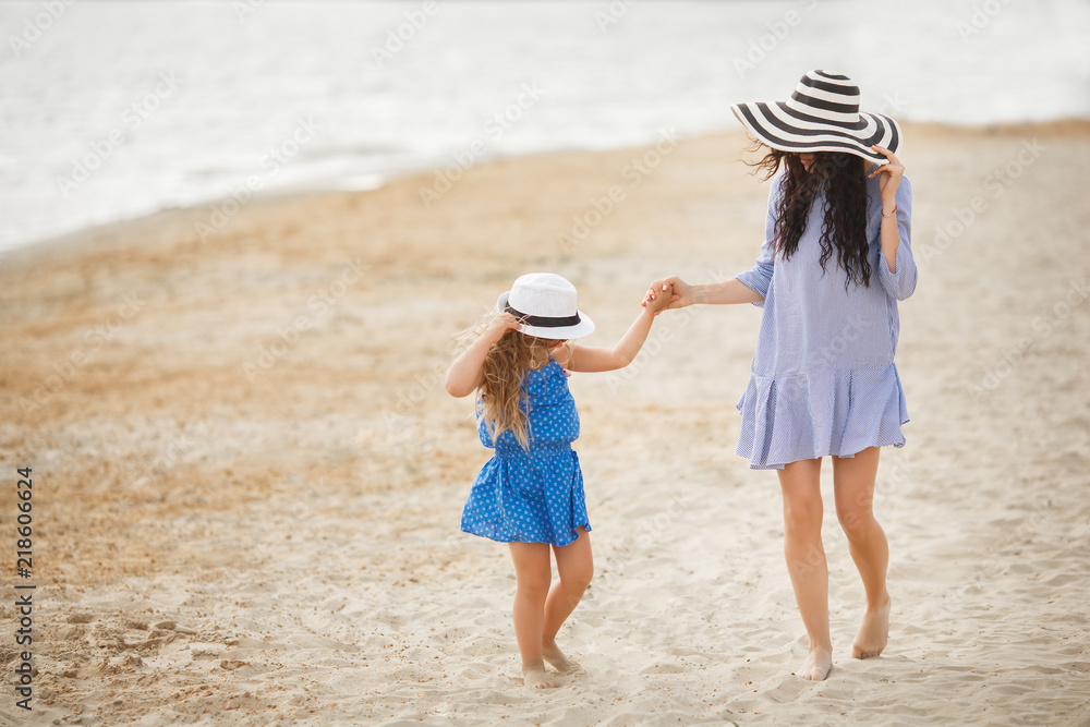 Mother and her little daughter having fun at the coast. Young pretty mom and her child playing near the water