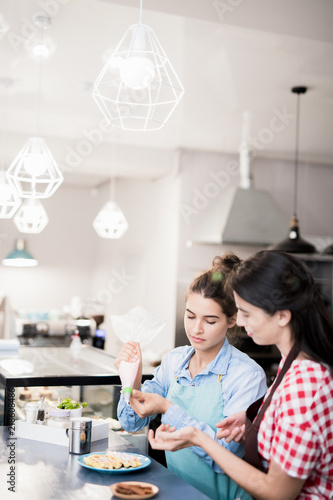 Waist up portrait of two young women pouring whipped cream over fresh waffles while preparing order in small cafe, copy space