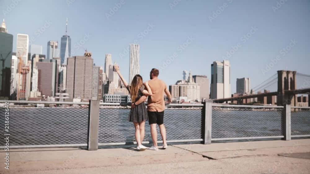 Happy Caucasian couple stand hugging, arms raised at amazing Manhattan skyline in New York, walk unimpressed slow motion Happy Caucasian couple stand hugging, arms raised at amazing Manhattan skyline in New York, walk unimpressed slow motion