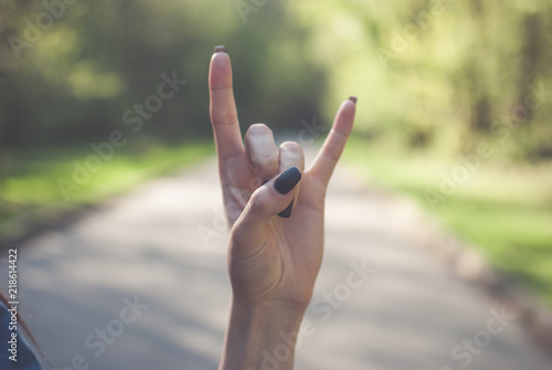 Girl making a sign of the horns gesture (satan's fingers) against sunny green background. © Yurii Zymovin
