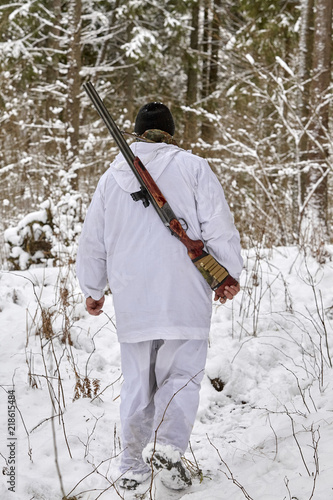 hunter in winter camouflage with shotgun in the forest photo