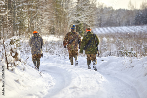 group of hunters in winter forest with carbines and shotgun photo