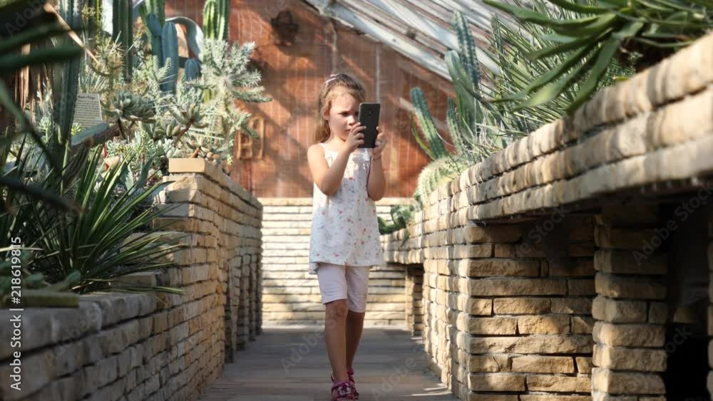 Child little girl takes mobile phone pictures of variety of cactus plants in a greenhouse of the botanical garden Child little girl takes mobile phone pictures of variety of cactus plants in a greenhouse of the botanical garden