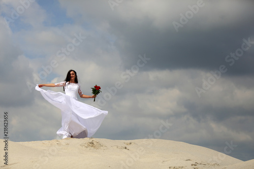 Ślub, wesele, piękna dziewczyna w białej sukni tańczy na szzycie piaszczystej wydmy.
