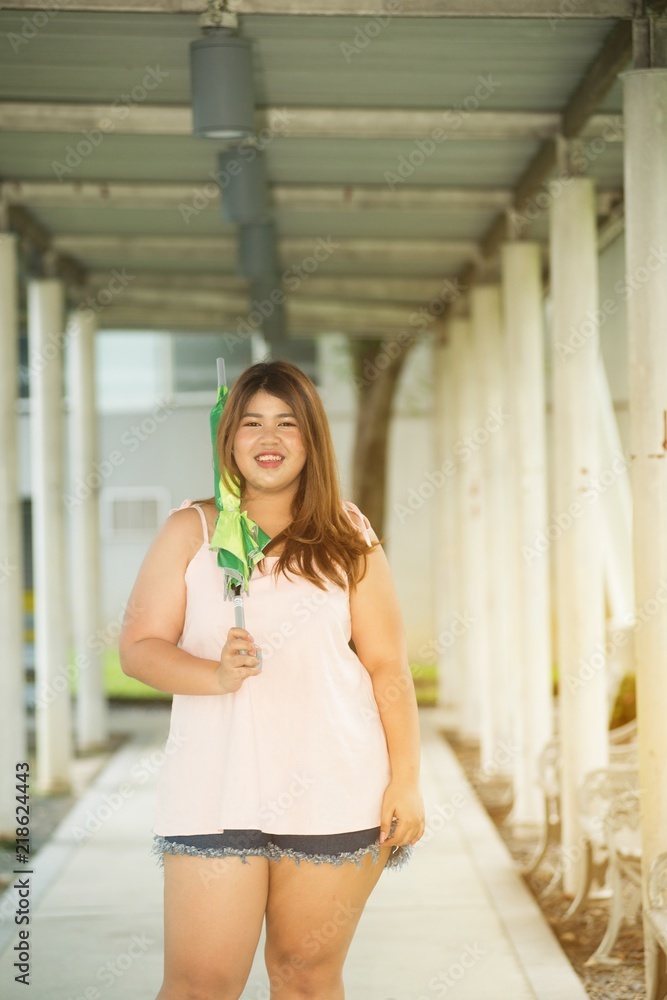 Asian pretty smiley face fat woman pose standing and hold umbrella on walkway. Asian pretty smiley face fat woman pose standing and hold umbrella on walkway.