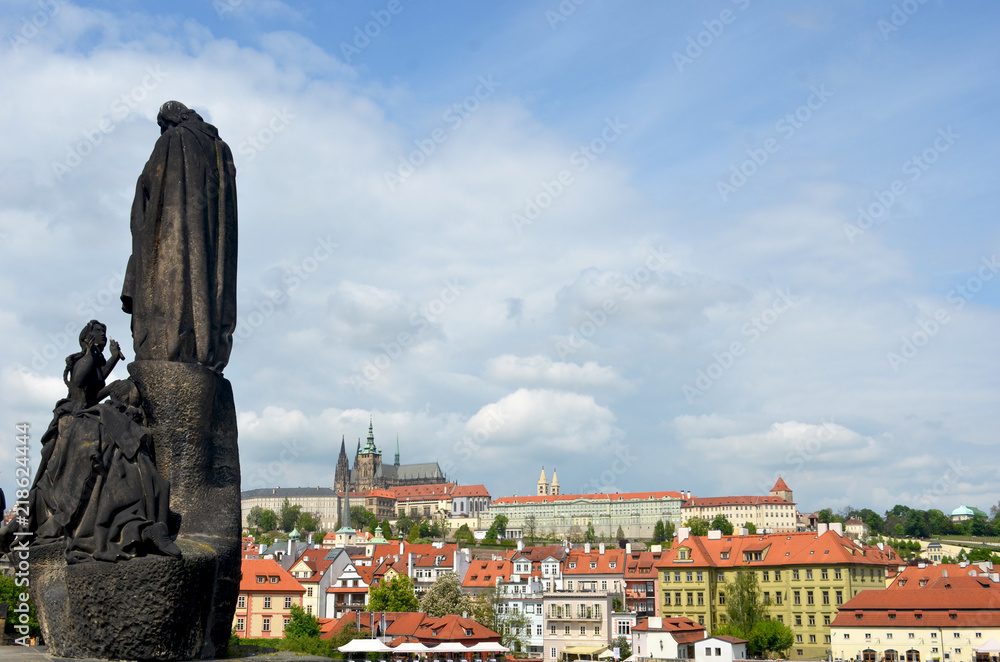A statue looks from the Charles Bridge towards Prague Castle. Storm clouds are gathering in the blue sky.