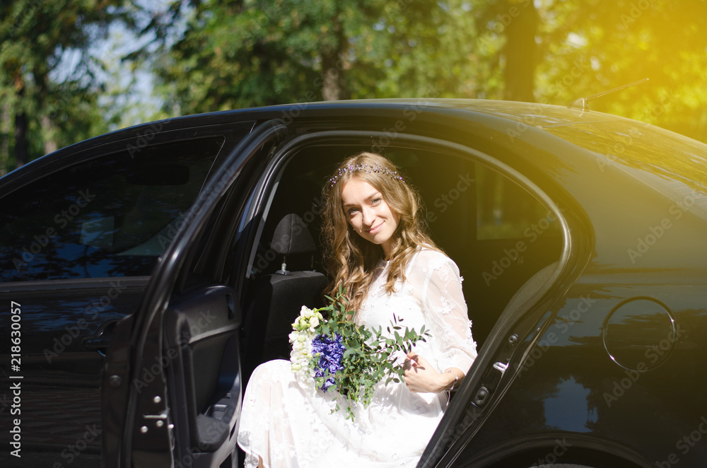 Bride in a white dress with a bouquet in the car sun nature