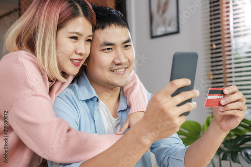 Asian couple use mobile phone shopping online with credit card together in living room at home.couple in home concept.