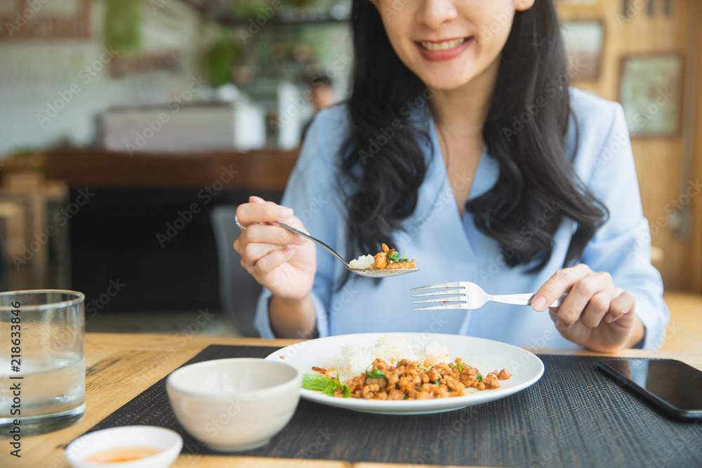 Close up young woman eating thai food in restaurant. Young woman eats pork with rice and vegetables at restaurant.