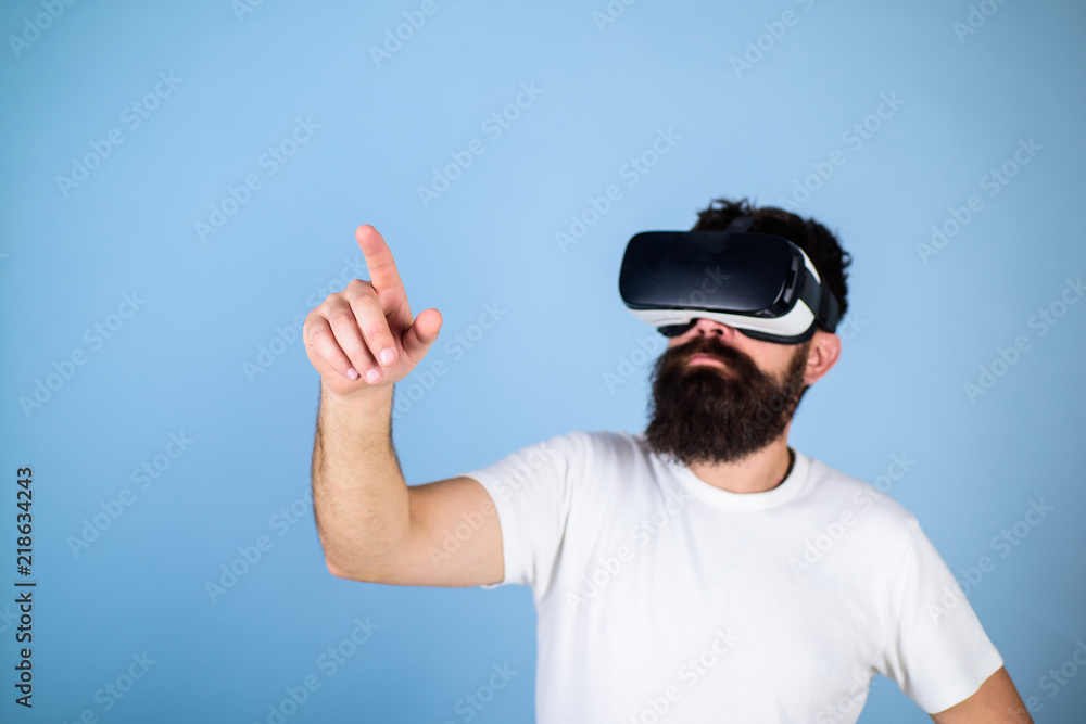 Man with beard in VR glasses, light blue background. Interactive surface concept. Guy with head mounted display interact in virtual reality. Hipster on busy face exploring virtual reality with gadget Man with beard in VR glasses, light blue background. Interactive surface concept. Guy with head mounted display interact in virtual reality. Hipster on busy face exploring virtual reality with gadget