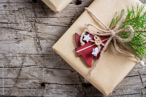 Holiday christmas gift box. Christmas present with fir branch and red wooden tree toy decoration on wooden table background. Top view, copy space