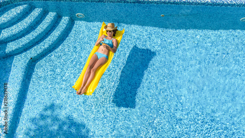 Beautiful young girl relaxing in swimming pool, swims on inflatable mattress and has fun in water on family vacation, tropical holiday resort, aerial top view from above 