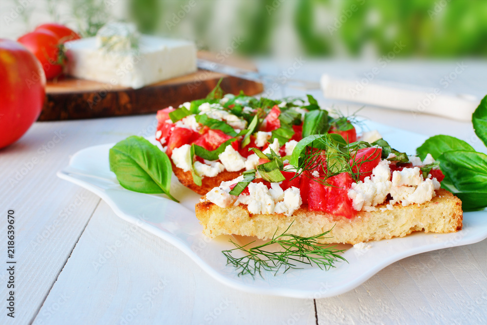 Tomato bruschettas with goat cheese and basil on plate over white wooden table Tomato bruschettas with goat cheese and basil on plate over white wooden table