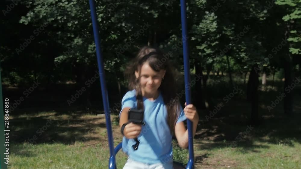 Child in the playground with an action camera. The girl on the swing shoots herself on the video camera. Child in the playground with an action camera. The girl on the swing shoots herself on the video camera.