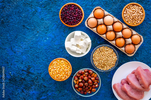 Food for sportsmen. Legumes, nuts, low-fat cheese, meet, eggs on blue background top view space for text