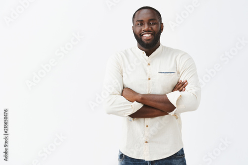 Satisfied African American man with beard looking and great result of personal efforts, being pleased and happy have great team, holding hands crossed on chest, standing in confident and carefree pose