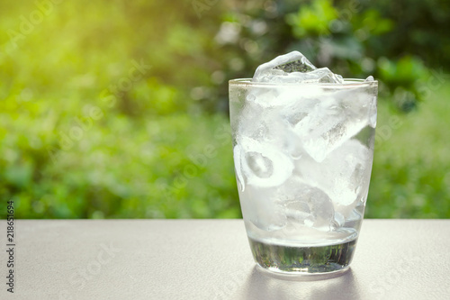 Glass of ice and water in put on table in the nature green background